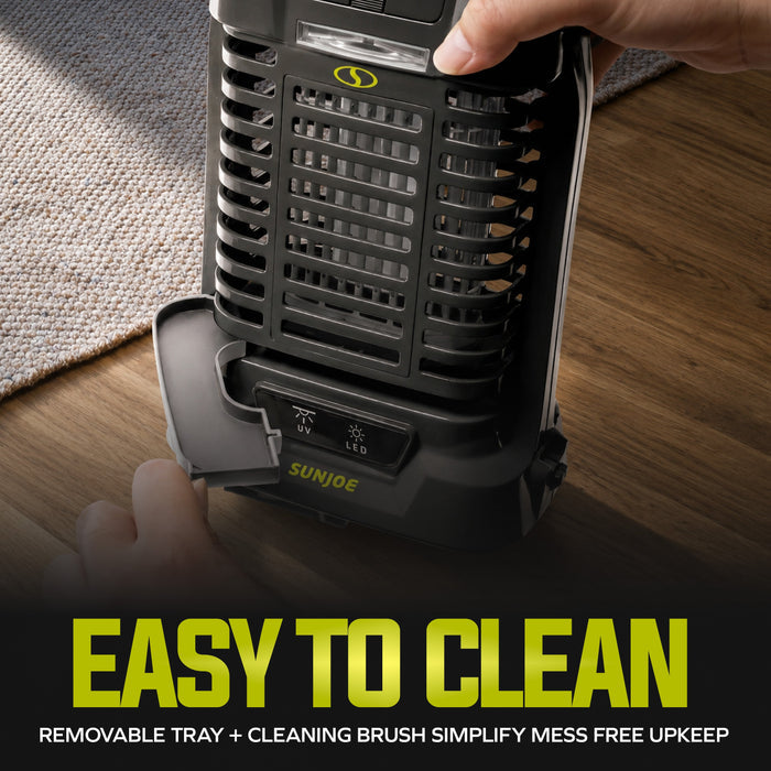 A handheld black and gray Sun Joe insect trap being held by a hand over a wooden floor, with a removable tray open at the base. Large text at the bottom reads 'EASY TO CLEAN' with smaller text about the removable tray and cleaning brush.