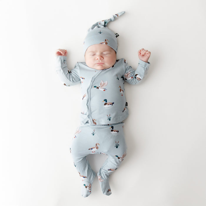 Sleeping newborn wearing the Take Me Home Set with Cap in Mallard Duck on a white surface