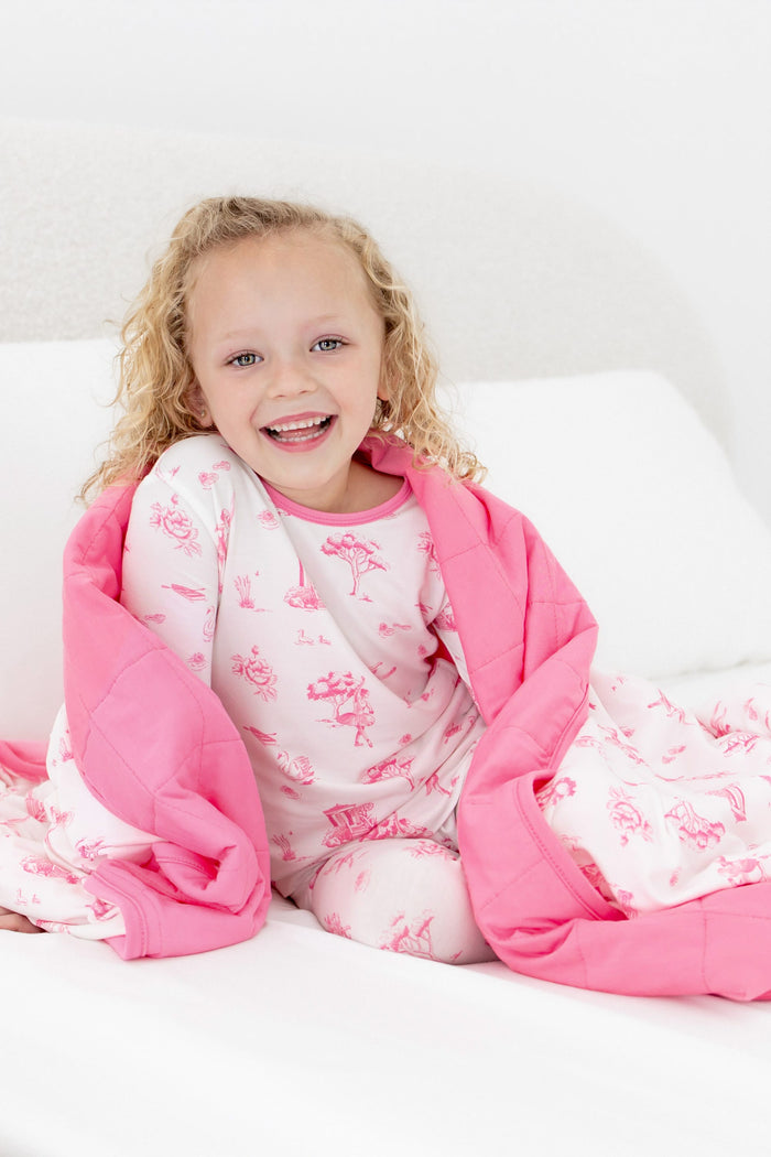 Close up of young girl sitting on a bed with the Toddler Blanket in Toile Ballet 1.0 around her shoulders