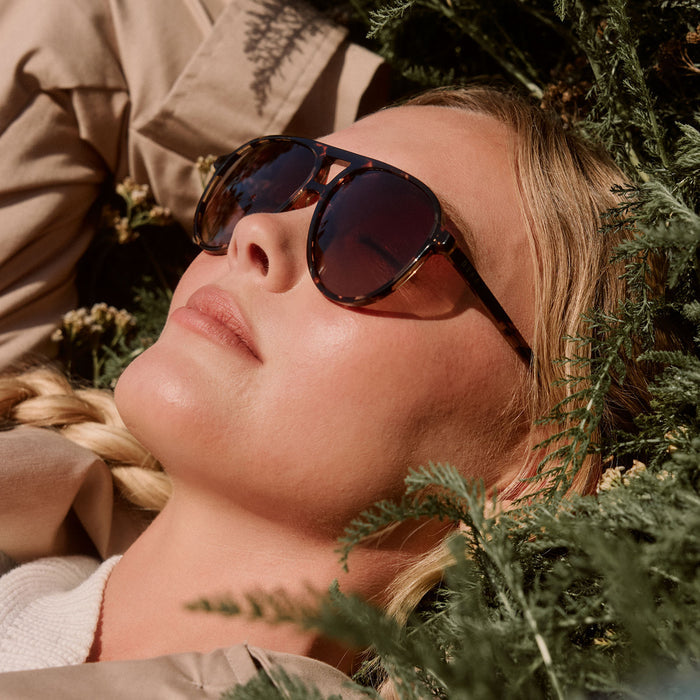 lifestyle - blonde female laying down in the sun wearing diff eyewear featuring the tosca ii aviator prescription glasses with a espresso tortoise frame side view