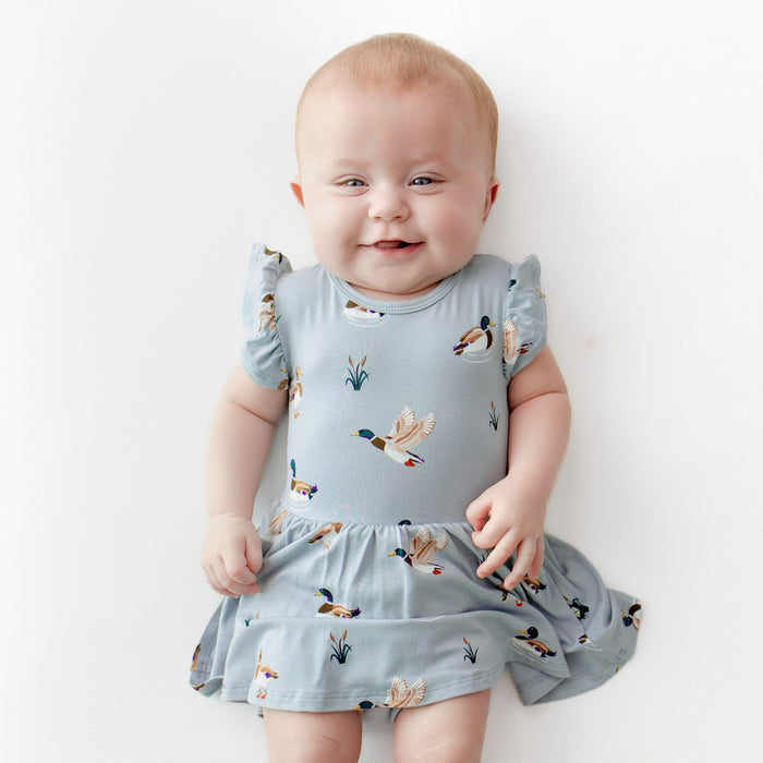 Close up of infant girl wearing the Twirl Bodysuit Dress in Mallard Duck laying on a white surface