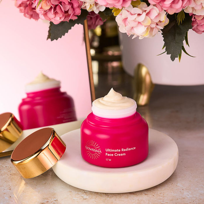 Pink face cream jar with gold cap on a marble coaster, surrounded by pink flowers.