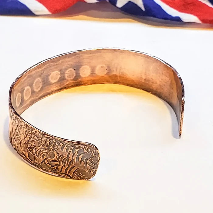 Copper cuff with embossed design on a white background