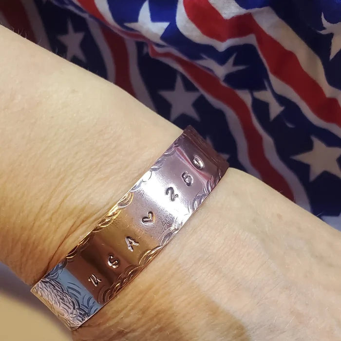 Copper bracelet with engraved USA 250 on a wrist against an American flag background