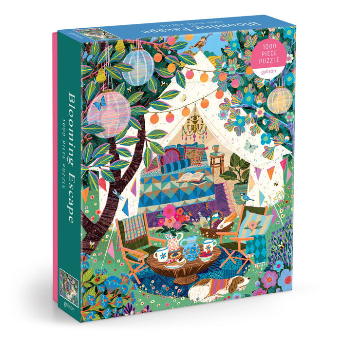 The Victoria Ball Blooming Escape 1000 Piece Puzzle by Victoria Ball features a cozy outdoor tent surrounded by flowers, plants, tea on a table, and colorful decorations in a vibrant garden.