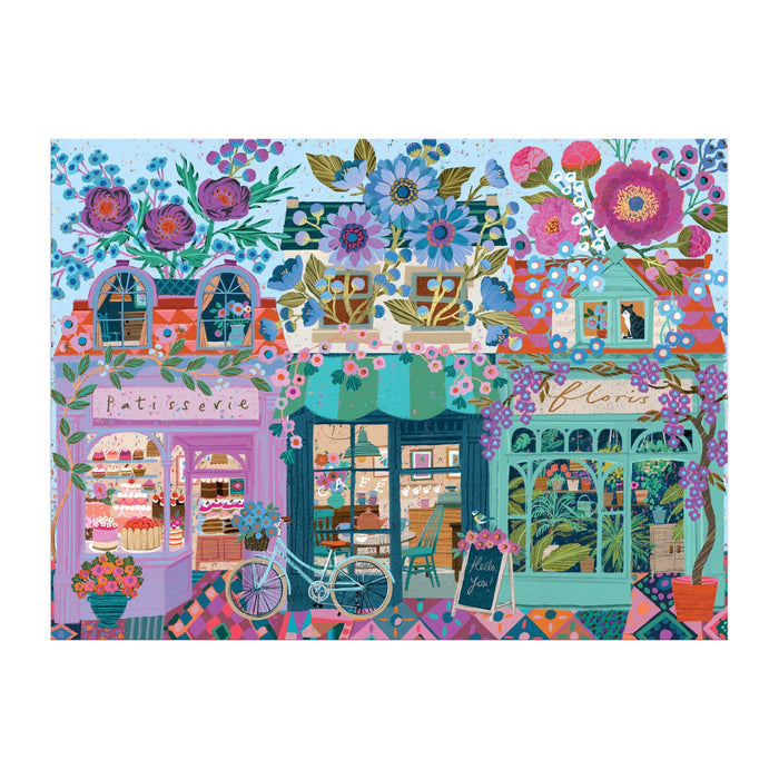 The Victoria Ball Open For Blossoms 1000 Piece Puzzle by Victoria Ball features vibrant, whimsical artwork of charming shops like a patisserie and florist, complete with flowers, pastries, a bicycle, and outdoor seating.