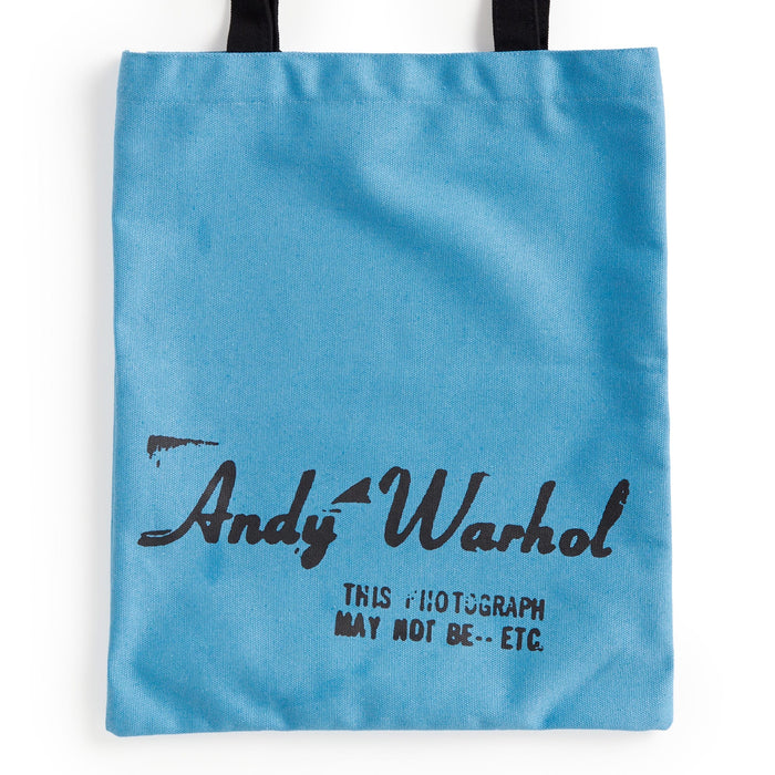 The Warhol Soup Can Volume 3 Canvas Tote Bag by the Andy Warhol Foundation features a light blue color, black handles, "Andy Warhol" in handwritten-style font, and "THIS PHOTOGRAPH MAY NOT BE..." printed below in black.