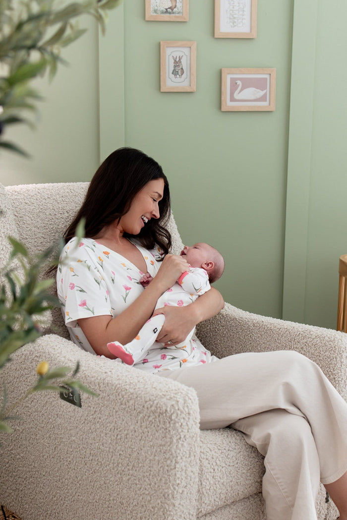 Mother sitting in a reclining chair wearing the Women's Relaxed Fit V-Neck in Tulip holding her newborn matching in a footie