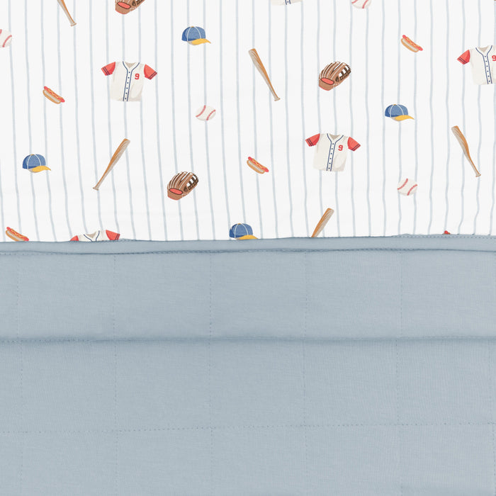 Close up of the Youth Blanket in Home Run 1.0 showing the muted blue quilted backing and smooth baseball print top layer