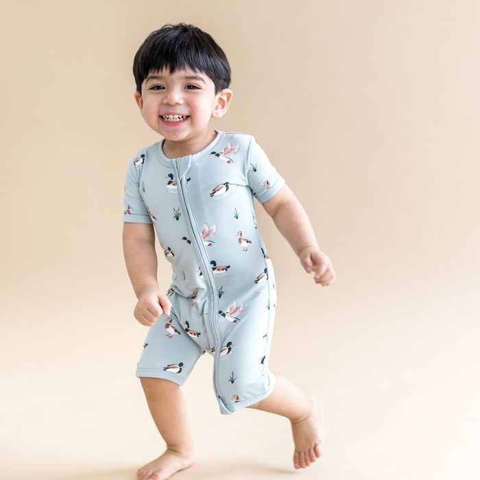 Young smiling boy walking wearing the Zipper Shortall Romper in Mallard Duck