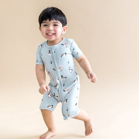 Young smiling boy walking wearing the Zipper Shortall Romper in Mallard Duck