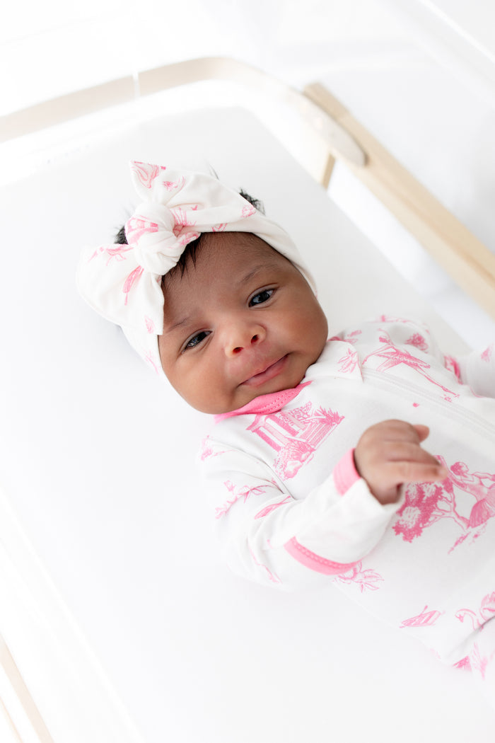 Newborn baby in a white crib with pink floral and ballet patterns and a matching headband.